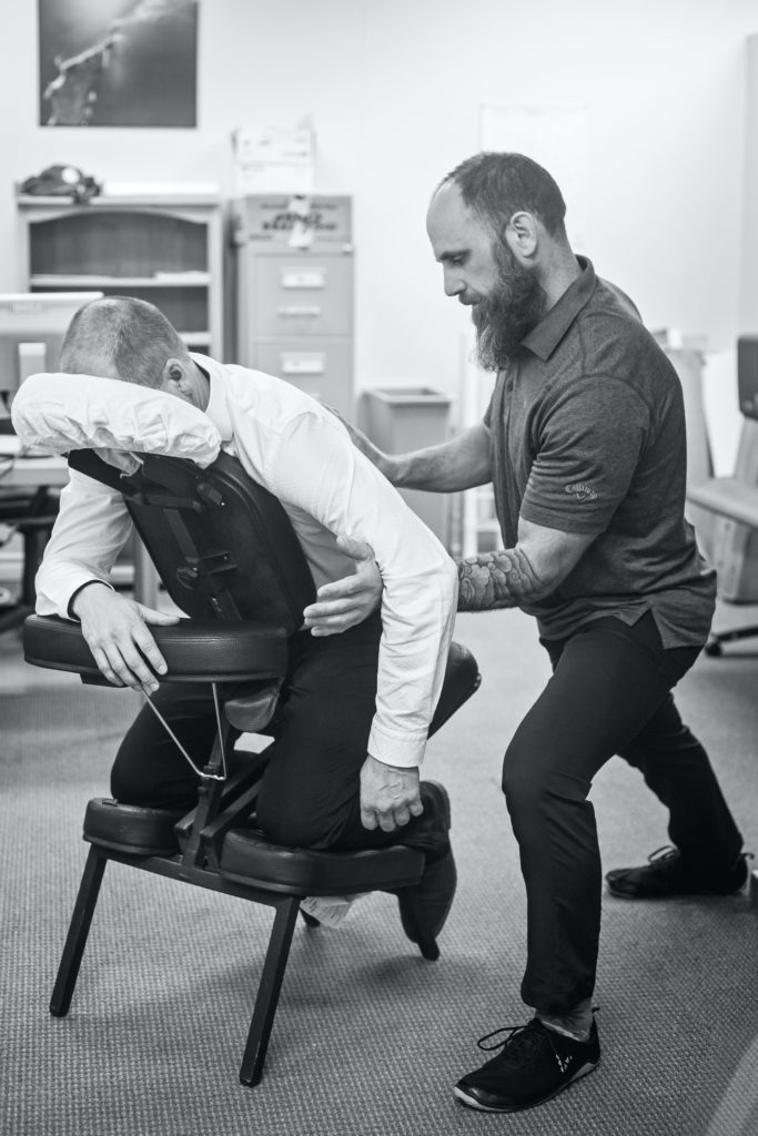 Male chiropractor doing an adjustment on a man in a chair